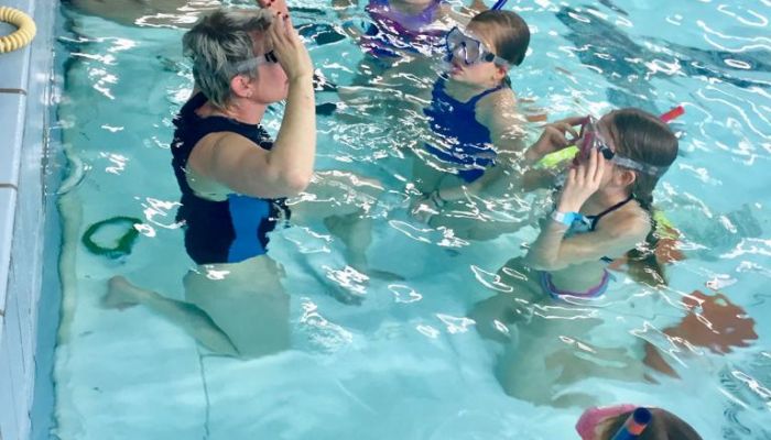 de zwemjuf laat aan 5 meiden zien hoe zij hun duikbril en snorkel op moeten zetten